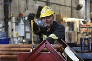Warehouse operator in a yellow hard hat cutting a strap on a bundle of steel bars.