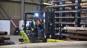 Warehouse forklift operator moving steel bar and tubes