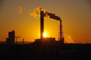 Sun setting behind an oil plant with a billow of rising smoke